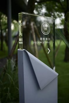 a clear glass award sitting on top of a metal post in the grass with trees behind it