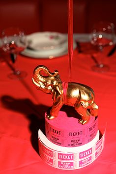 an elephant shaped ticket holder on top of a red table cloth with silver place settings