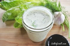 a jar filled with dressing sitting on top of a wooden table next to lettuce