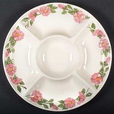 a white plate with pink flowers and green leaves on the rim, sitting on a black surface