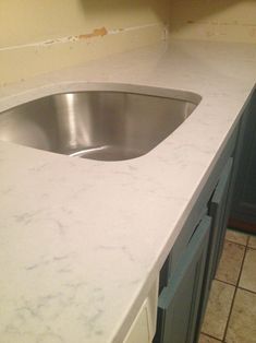 a white counter top with a silver sink in the middle and tile floor next to it