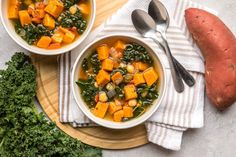 two bowls of vegetable soup on top of a wooden plate next to a sweet potato