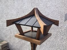 a small wooden bird feeder on top of a cement ground next to a building with a window