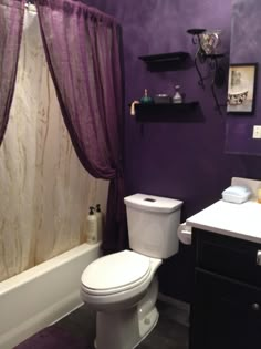 a white toilet sitting next to a bath tub under a purple curtain in a bathroom