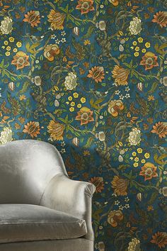 a chair sitting in front of a blue wallpaper with flowers and leaves on it