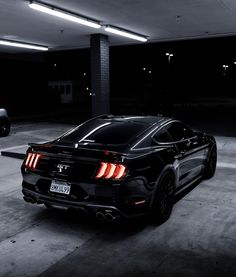 a black sports car parked in a parking garage with its rear lights turned on at night