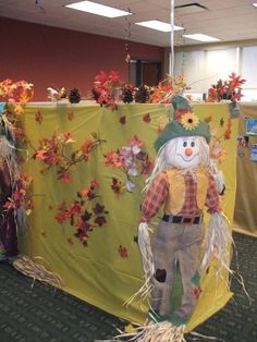 a scarecrow is standing in front of a table covered with fall leaves and decorations