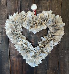 a heart shaped wreath made out of old newspaper pages with a white teddy bear on top