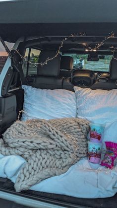 the back of a truck with blankets and pillows in it's trunk, along with other items