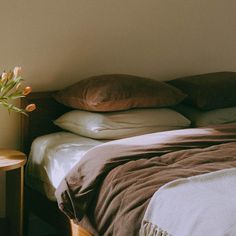 a bed with brown sheets and pillows on top of it next to a small table