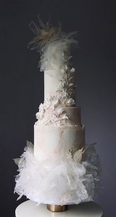 a three tiered wedding cake with white flowers and feathers