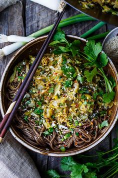 a bowl filled with noodles, vegetables and chopsticks on top of a wooden table