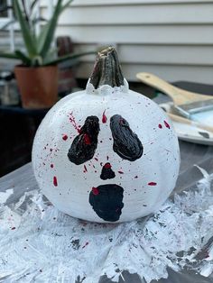 a white painted pumpkin with black and red paint splattered on it's face