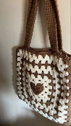 a brown and white crocheted bag hanging from a hook on the side of a wall