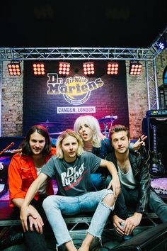 four people sitting on top of a motorcycle in front of a brick wall and stage