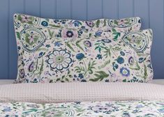 a bed with blue and green flowers on the pillowcase, next to a wall