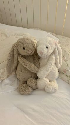 two stuffed animals sitting next to each other on top of a white bedspread