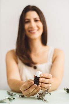 a woman sitting at a table holding a bottle with flowers around her and smiling for the camera