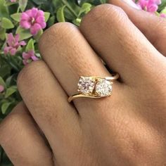 a woman's hand holding a ring with two stones on it and pink flowers in the background