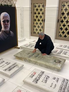 a man kneeling down in front of some writing on the ground next to a painting