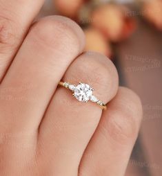 a woman's hand holding an engagement ring with three stones on it and the middle finger