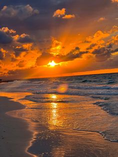 the sun is setting over the ocean with clouds in the sky and water on the beach