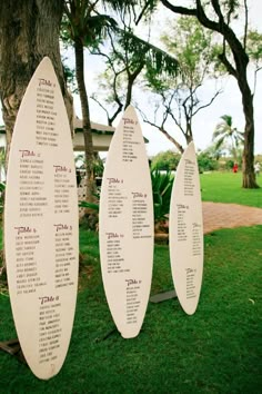 three surfboards with seating cards on them sitting in the grass next to a tree