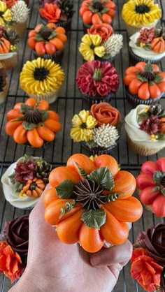 a person holding up a fake flower in front of cupcakes on a rack