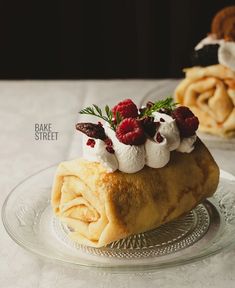 a pastry with raspberries and whipped cream on top sits on a glass plate