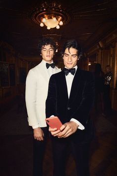 two men in tuxedos are standing next to each other holding an electronic device