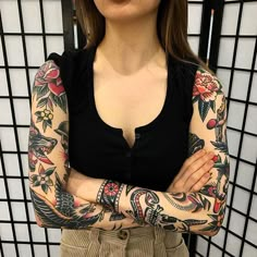 a woman with tattoos on her arms standing in front of a tiled wall