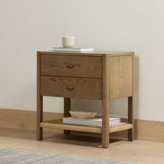 a small wooden table with two drawers and a cup on top of the shelf next to it