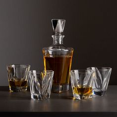 an assortment of whiskey glasses and a decanter on a dark table with a gray background