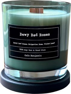 a candle that is sitting on top of a wooden stand and has a label reading dewy red roses