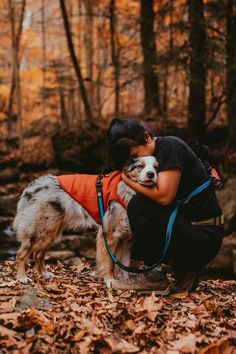 a woman hugging her dog in the woods with autumn leaves on the ground around her