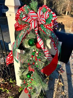 a christmas wreath is hanging on the mailbox in front of a mailbox with red, green and white bows