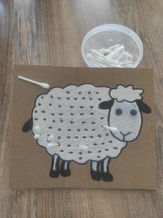 a sheep is drawn on a piece of brown paper next to a cup of white string