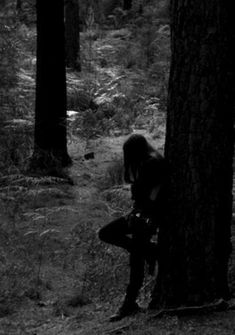 a woman is sitting on a tree in the middle of a forest with her back turned to the camera