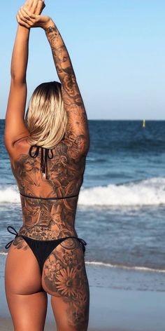 a woman with tattoos on her back standing in front of the ocean