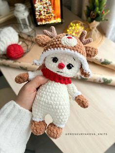 a hand holding a small stuffed animal wearing a knitted hat and scarf on top of a table