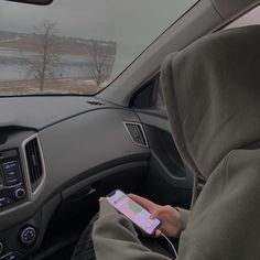 a person sitting in the passenger seat of a car holding a cell phone and wearing a hoodie