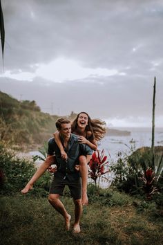 a man carrying a woman on his back in the middle of a field by the ocean