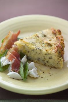 a piece of quiche on a yellow plate with bacon and feta cheeses