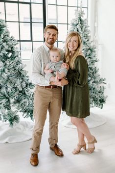 a man and woman holding a baby in front of christmas trees