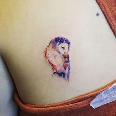 a small owl tattoo on the back of a woman's left shoulder and stomach