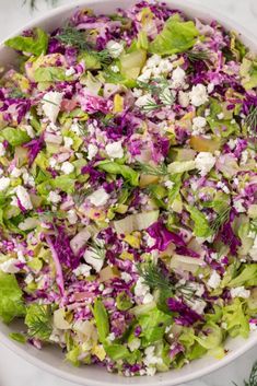 a white bowl filled with lettuce, red cabbage and feta cheese salad