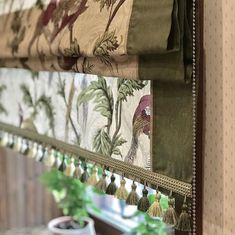 a window with curtains and tassels hanging from it's sides, in front of a potted plant