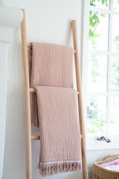 a pink towel hanging on a wooden ladder next to a basket and window in a white room