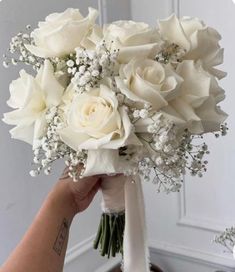 a bouquet of white roses and baby's breath is being held by a woman