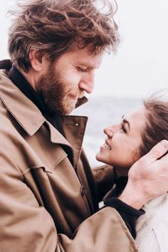 a man and woman standing next to each other near the ocean with their arms around each other